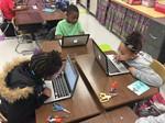 Three elementary students sitting at desks working on laptops 